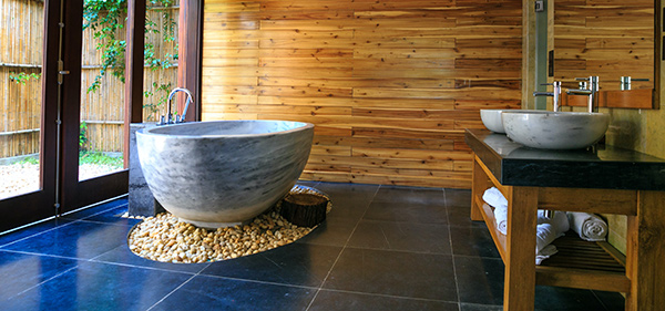 Home builder Westifeld shows bathroom with wooden wall, marbled stone tub which is sitting on pile of loose marble surrounded by dark blue large floor tiles.